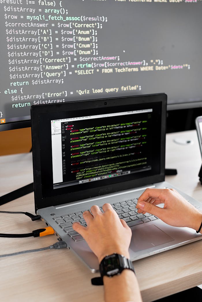 gallery-5 Person coding at a desk with laptop and external monitor showing programming code.